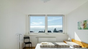 Une chambre avec deux lits, une chaise, un radiateur et une fenêtre donnant sur la ville.