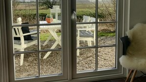 Ein Zimmer mit einer Schiebetür zu einem Sitzbereich im Freien mit weißen Möbeln und Blick auf einen Garten.