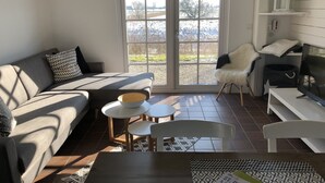 Ein Wohnzimmer mit einer Couch, einem Couchtisch, einem Sessel und einem Fernseher. Ein Fenster bietet Blick auf eine verschneite Landschaft.