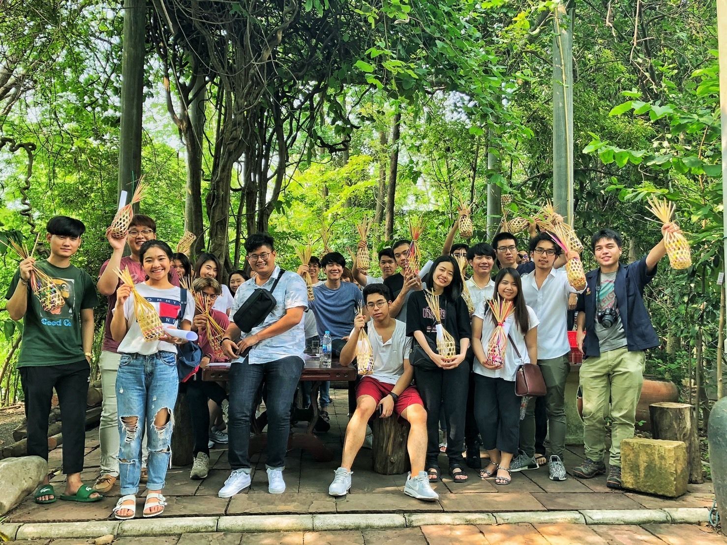 A group of people outdoors, some holding items, with trees and greenery in the background.