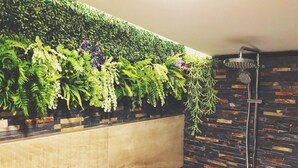 A bathroom with a vertical garden, a shower, and a tiled wall.