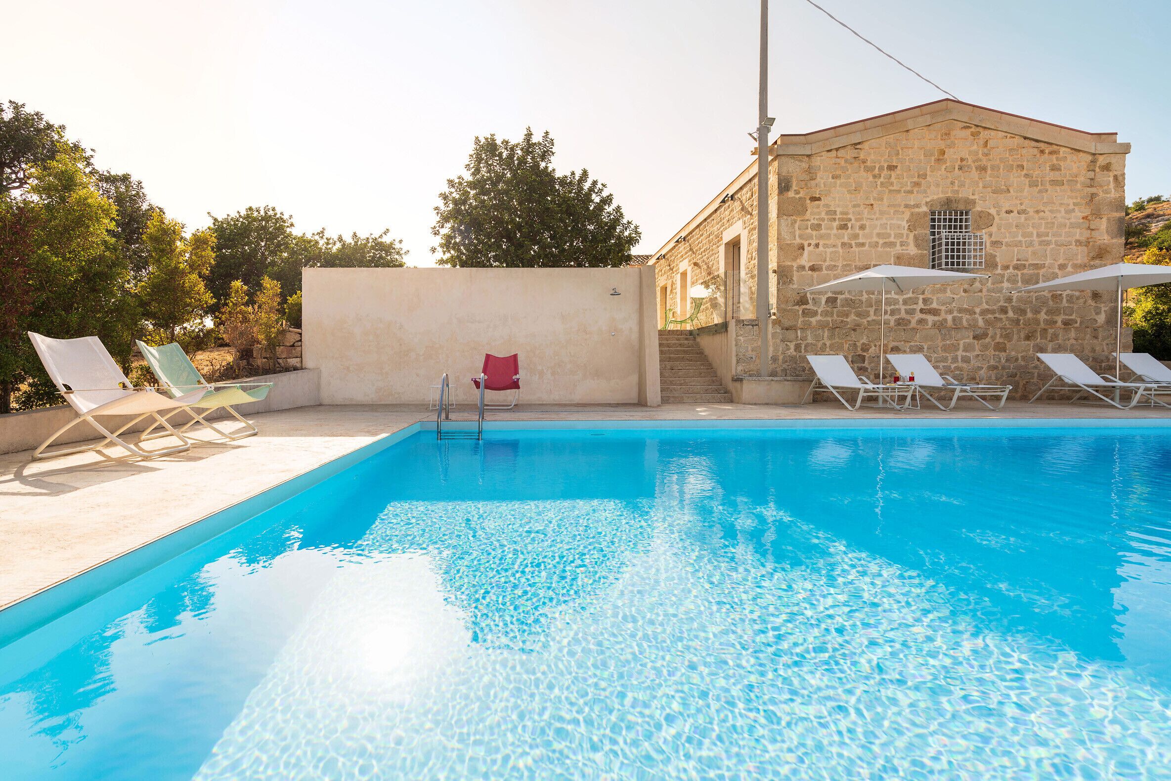 Une piscine avec des chaises longues et, en arrière-plan, un bâtiment en pierre.