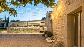 An outdoor patio with stone flooring, green chairs, a table with a bottle, and string lights. - Villa with pool and private wellness area in Scicli, Sicily - 8 pax (Scicli)