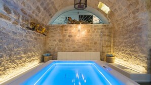 A stone-walled room with a large, illuminated swimming pool, a bench, and a small statue. - Villa with pool and private wellness area in Scicli, Sicily - 8 pax (Scicli)