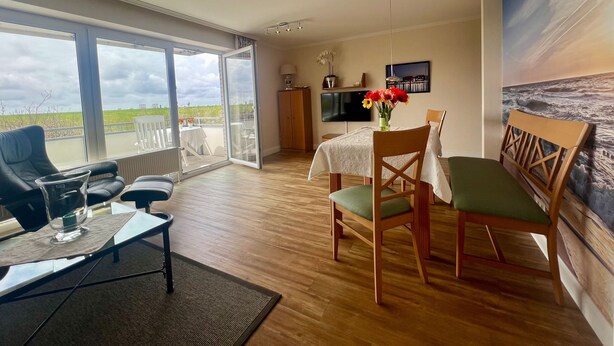 A modern living room with a dining area, large windows, and a view of the sea.