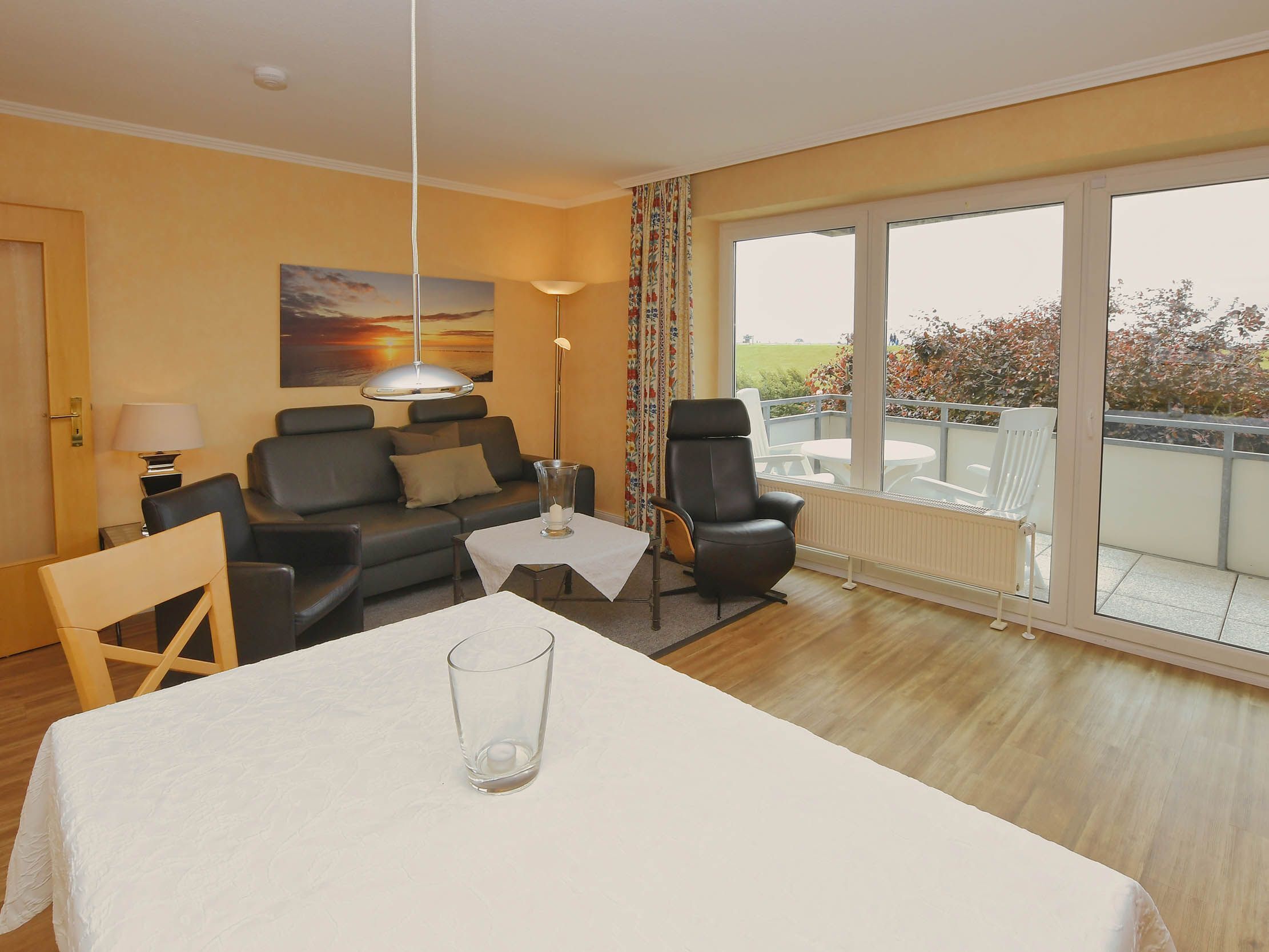 A modern living room with a sofa, a dining table, and a balcony with a view.