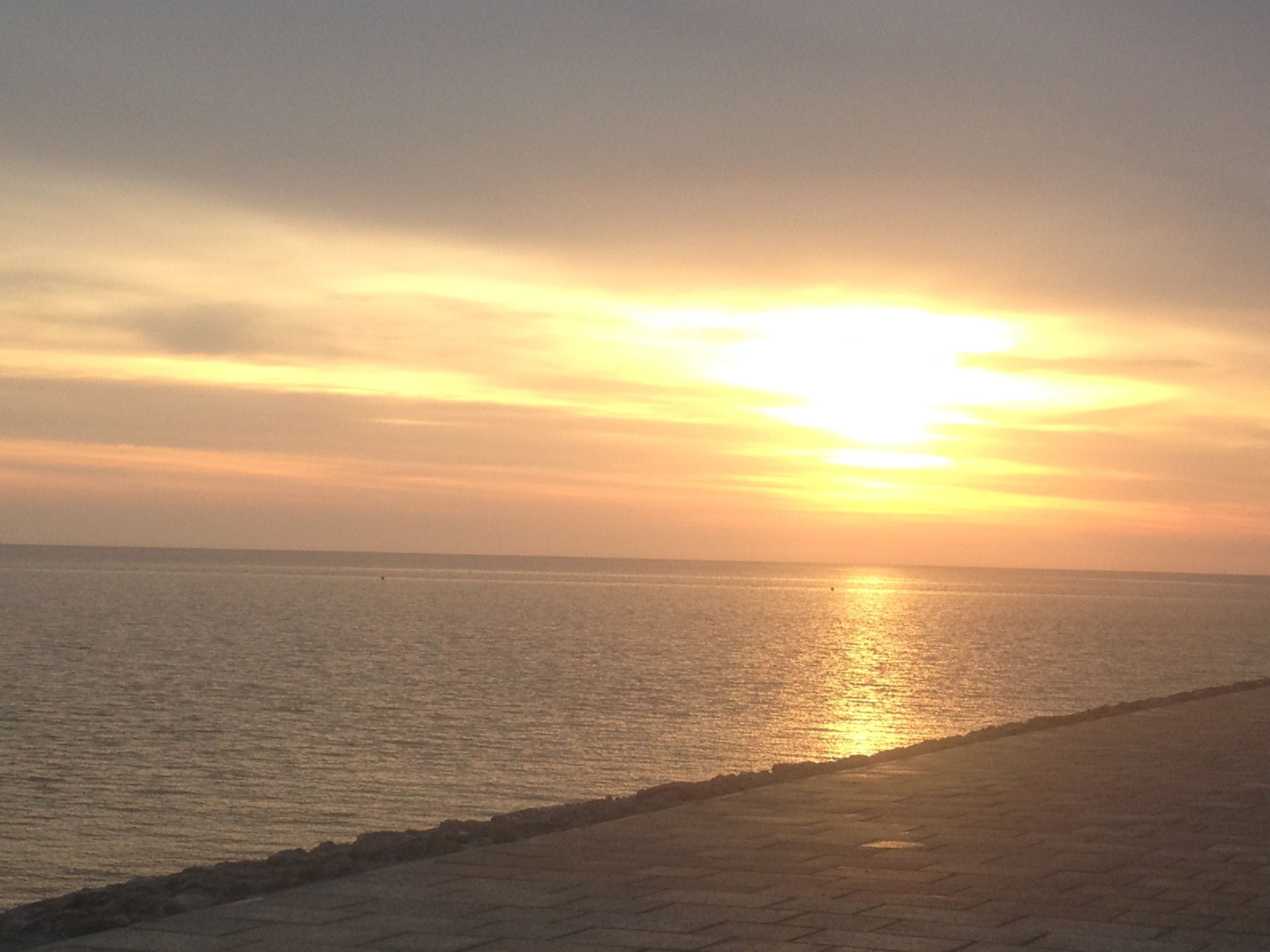 Un coucher de soleil sur une mer calme, avec une promenade pavée longeant la côte.