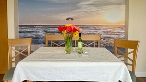 A dining table with a white tablecloth, two wooden chairs, a bottle of wine, and a vase of flowers.