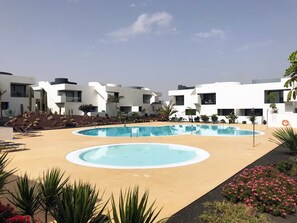 Ett modernt semesterkomplex med två pooler, omgivet av vita byggnader och vackert anlagda trädgårdar.