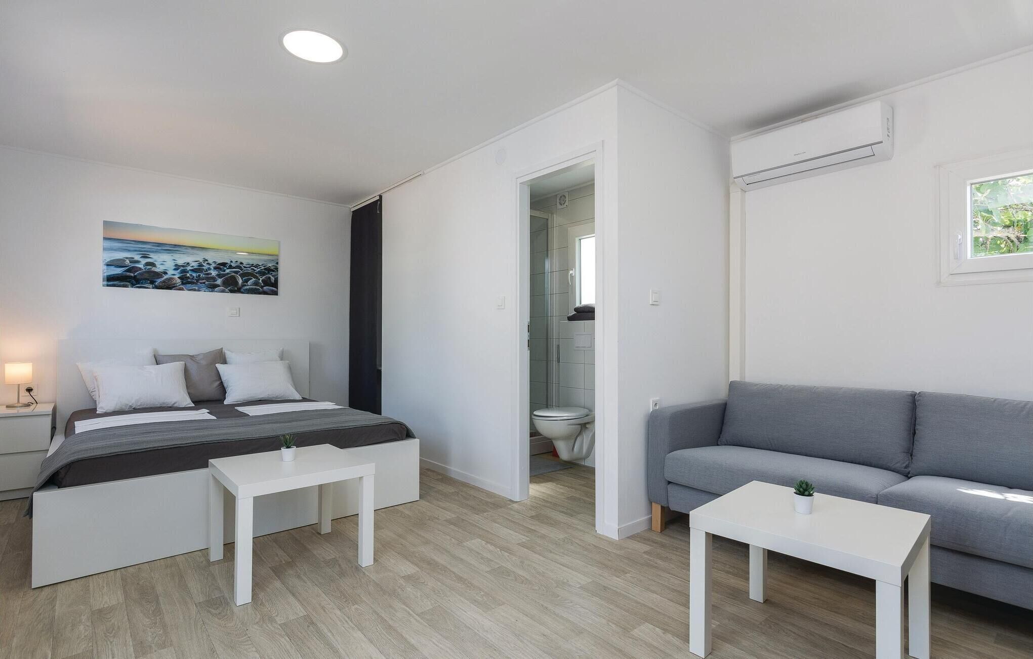 A modern, minimalist bedroom with a bed, bedside tables, a grey sofa, and a small table.