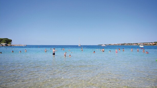 Una spiaggia con acque limpide e poco profonde, e una barca a vela all'orizzonte.