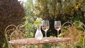 Une table en métal, avec deux verres à vin et un vase de fleurs, dans un décor de jardin.