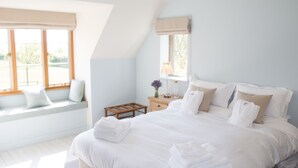 Une chambre avec un grand lit, un coin fenêtre aménagé en siège et une petite table en bois avec une lampe.