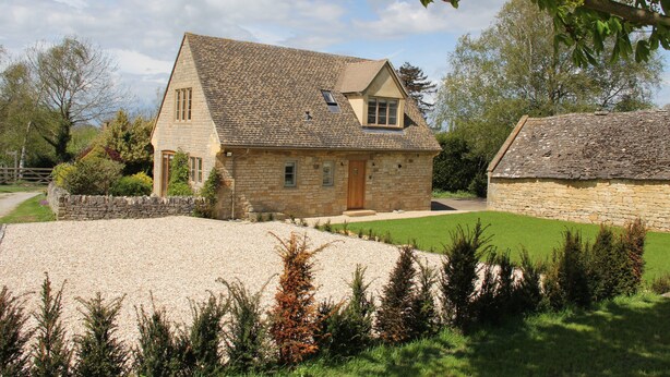 Une maison en pierre avec un toit en pente, une allée gravillonnée et une pelouse bien entretenue.