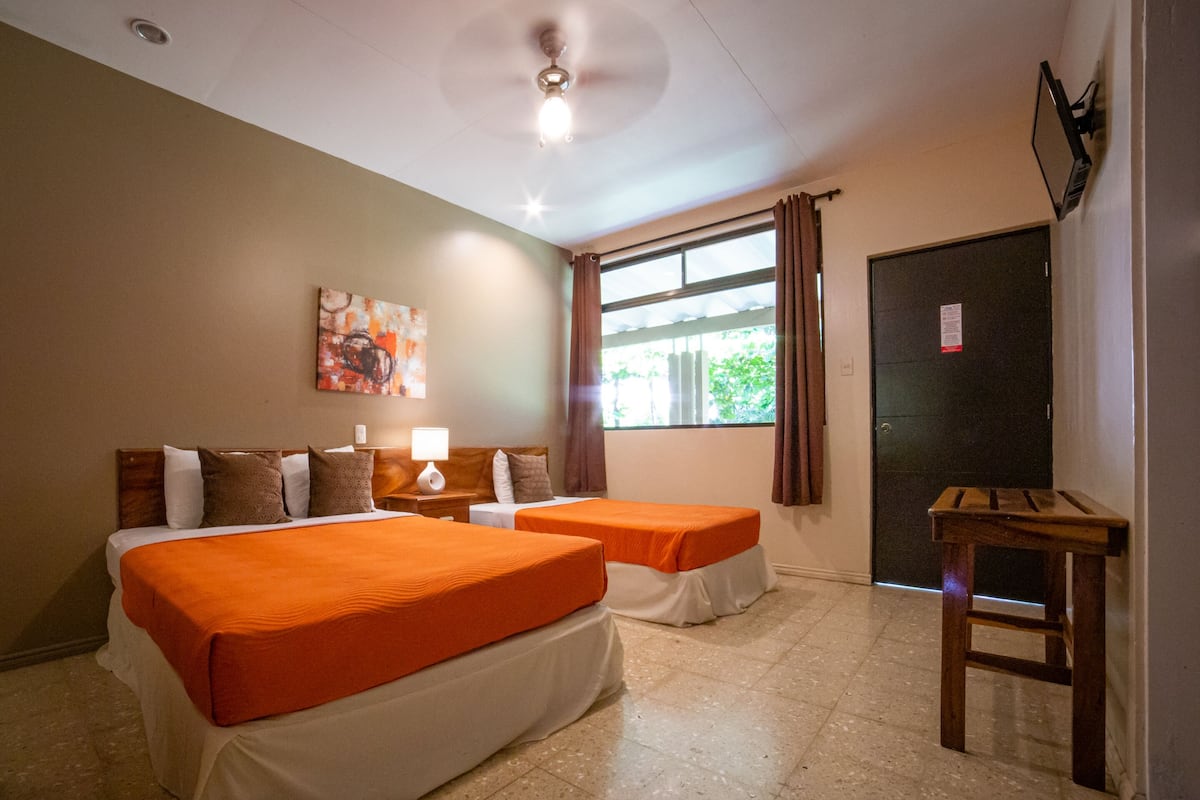A hotel room with two beds, a ceiling fan, a window with curtains, and a door.