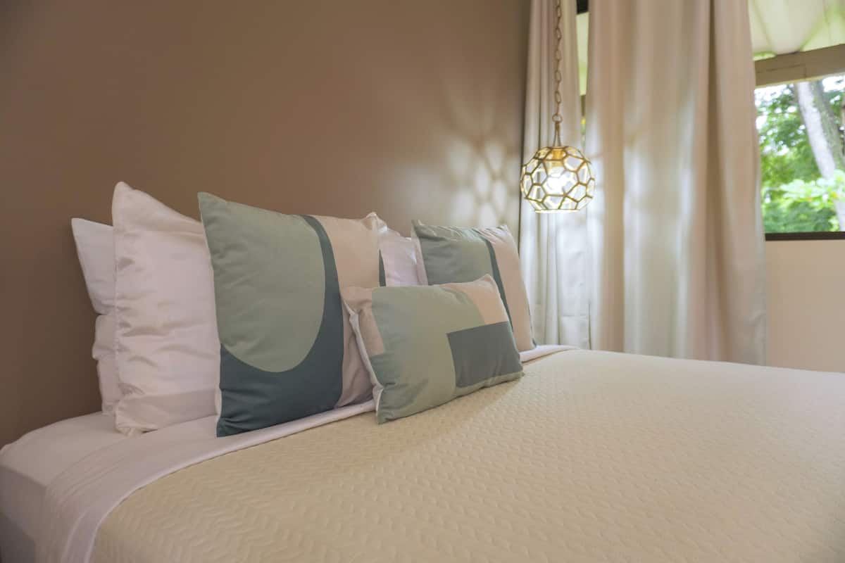 A neatly made bed with a quilted cover and several pillows in shades of white and green.