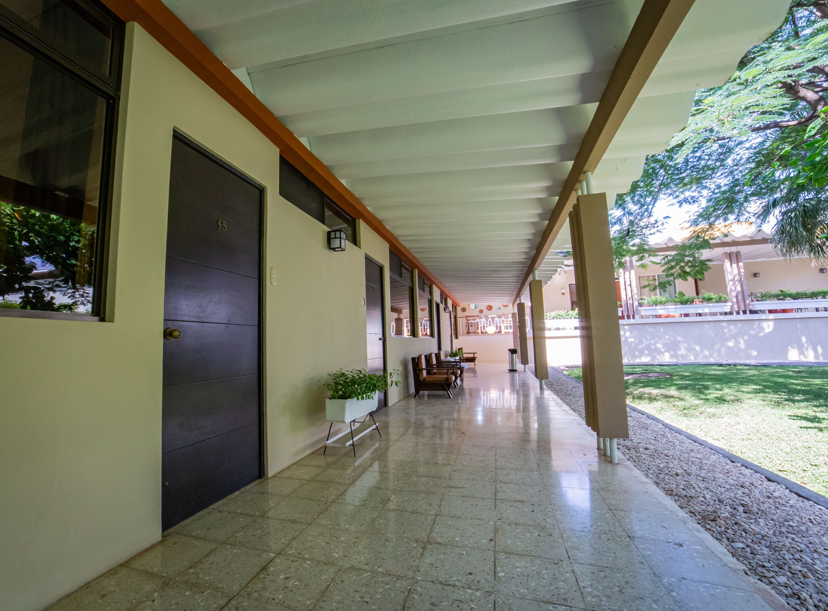 A covered corridor with tiled flooring, a bench, and potted plants.