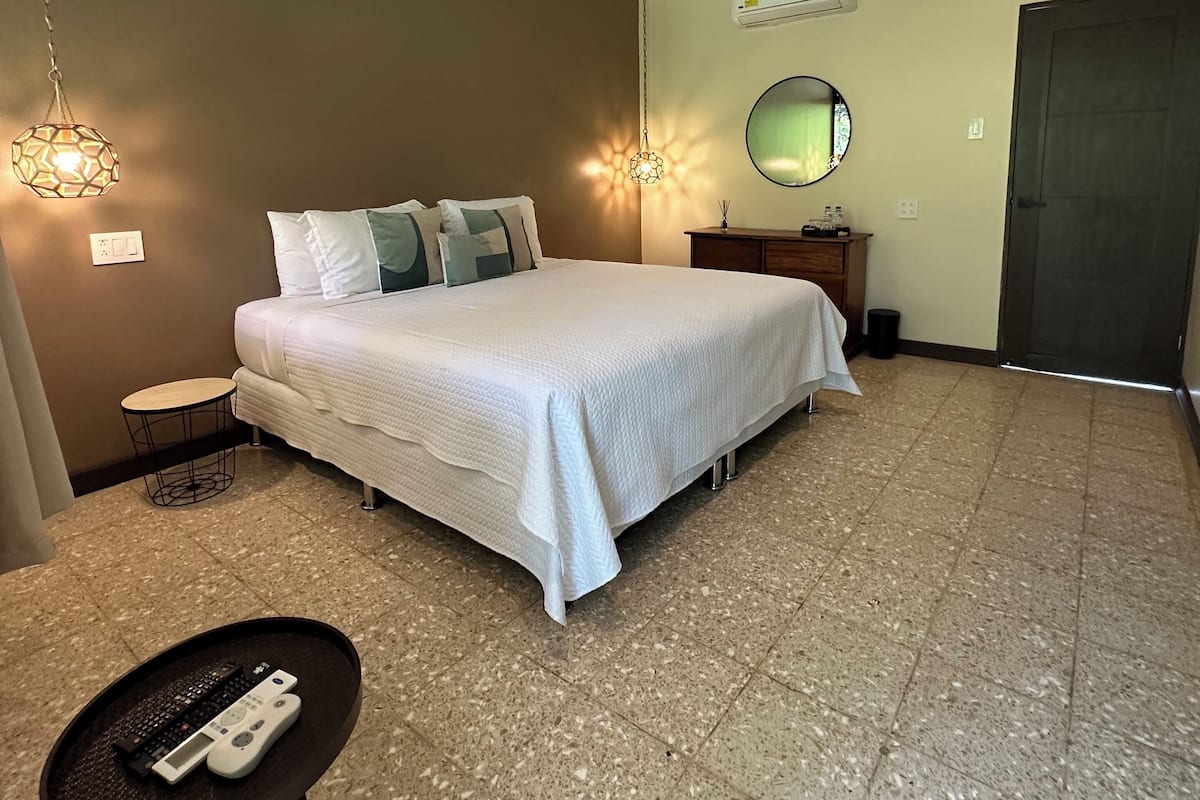 A bedroom with a bed, a ceiling fan, a round mirror, and a small table with a keyboard.