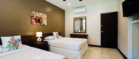 Une chambre d’hôtel avec deux lits, un ventilateur de plafond, un tableau au mur, un appareil de climatisation, un miroir et un téléviseur.