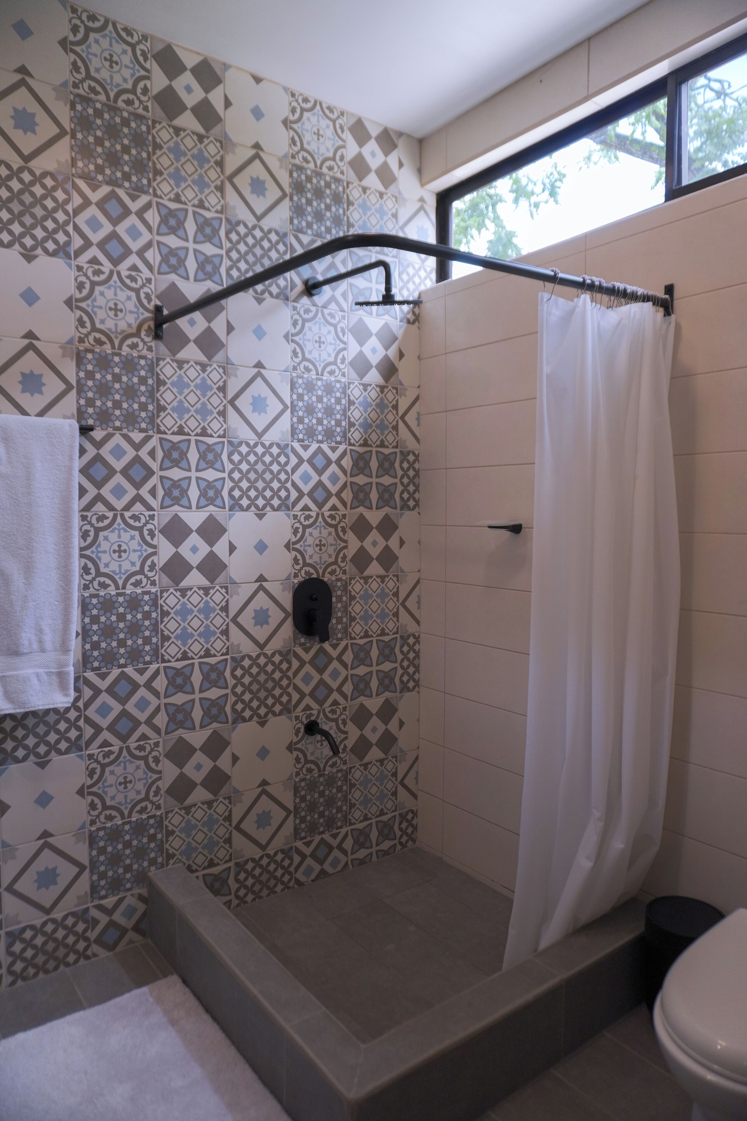 Et badeværelse med et mønstret flisegulv, en bruser med badeforhæng og et toilet.