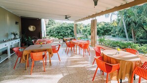 An outdoor dining area with red chairs and tables, a ceiling fan, and a view of lush greenery. - Hotel Diriá Santa Cruz (Santa Cruz)