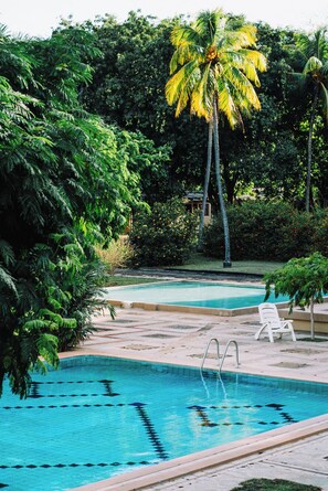 A swimming pool with clear blue water, surrounded by lush greenery and palm trees. - Hotel Diriá Santa Cruz (Santa Cruz)