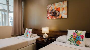 A hotel room with two beds, a nightstand with a lamp, a floral pillow, and a painting on the wall.