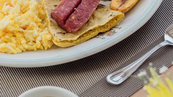 Um prato com arroz, ovos mexidos, presunto, banana frita e uma xícara de café preto.