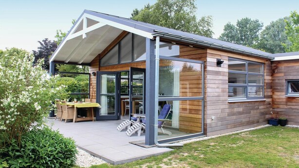 A modern house with a large glass door, a covered patio, and a wooden exterior.