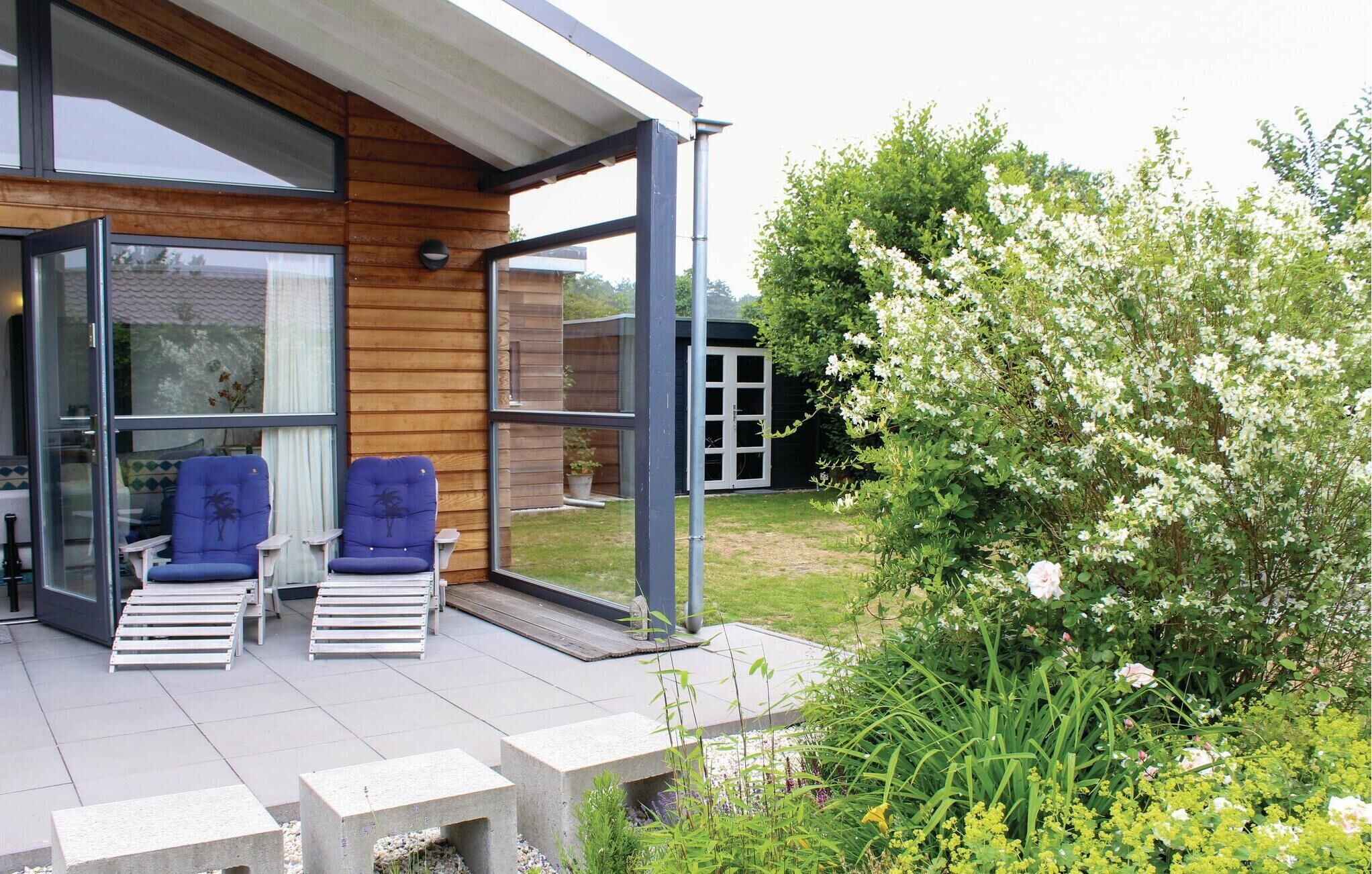 Ein modernes Haus mit Holzfassade, einem Glastür-Eingang und einer Terrasse mit zwei blauen Stühlen und einem kleinen Tisch.