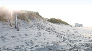 A sandy beach with a dune, a lifeguard tower, and a beach hut.