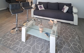 Ein modernes Wohnzimmer mit einem Glastisch, einer Couch und zwei Barhocker.