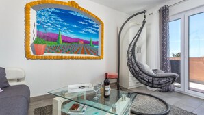 Una sala moderna con una mesa de centro de vidrio, un sofá, una silla colgante y un cuadro grande enmarcado.