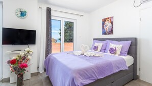 Un dormitorio con cama, televisión, un cuadro y ventana.