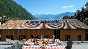 Un coin repas avec une table dressée pour le repas, des panneaux solaires sur le toit et un paysage montagneux en arrière-plan.