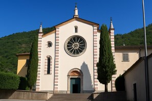 A church with a central circular window, a bell tower, and a cross on top. - Residence Eden Gardenia 9, Argegno, Italy (Argegno)