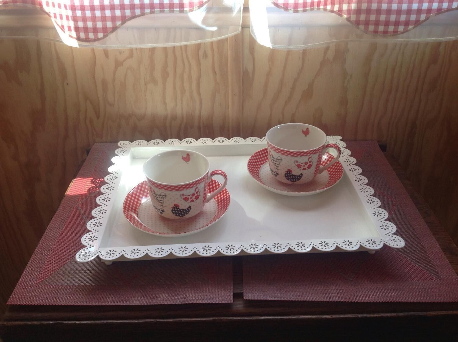 Two cups and saucers on a tray with a lace doily, placed on a table with a red and white checkered tablecloth.