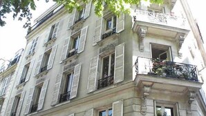 A multi-story building with white facades, multiple windows with shutters, and balconies with wrought iron railings.