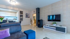 A modern living room with a grey sofa, a blue ottoman, a flat-screen TV mounted on a wall, and a white entertainment unit. - Lovely home in Dicmo with sauna (Dicmo)