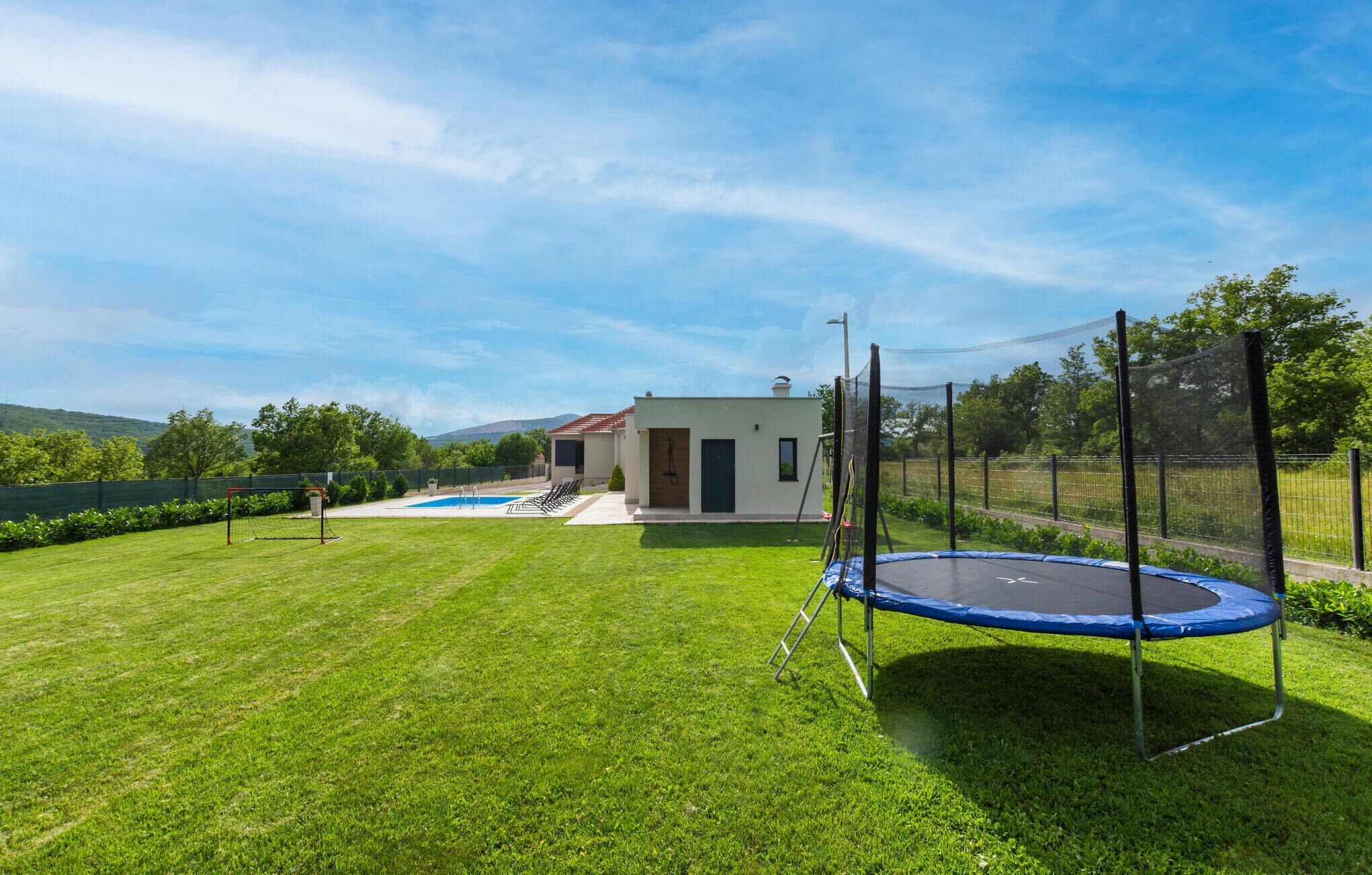 A well-maintained backyard with a swimming pool, a trampoline, and a small house.
