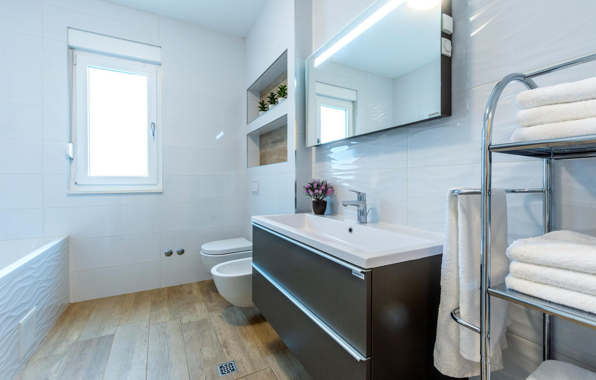 Un baño moderno con un lavabo blanco, un inodoro, un bidé y un perchero para toallas.