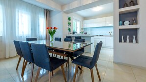 A modern dining area with a glass table and blue chairs, a kitchen with white cabinets, and a shelf with decorative items. - Lovely home in Dicmo with sauna (Dicmo)