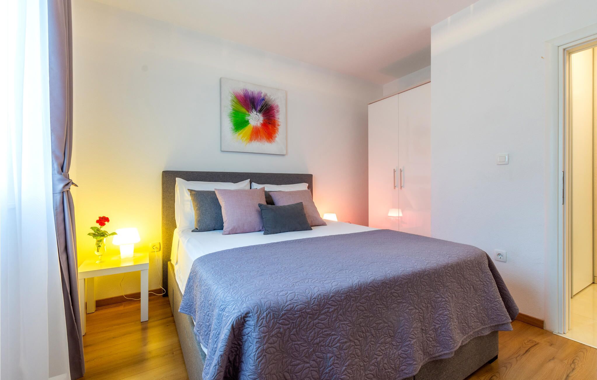 Ein ordentlich eingerichtetes Schlafzimmer mit Bett, Nachttisch und einem farbenfrohen, abstrakten Gemälde an der Wand.