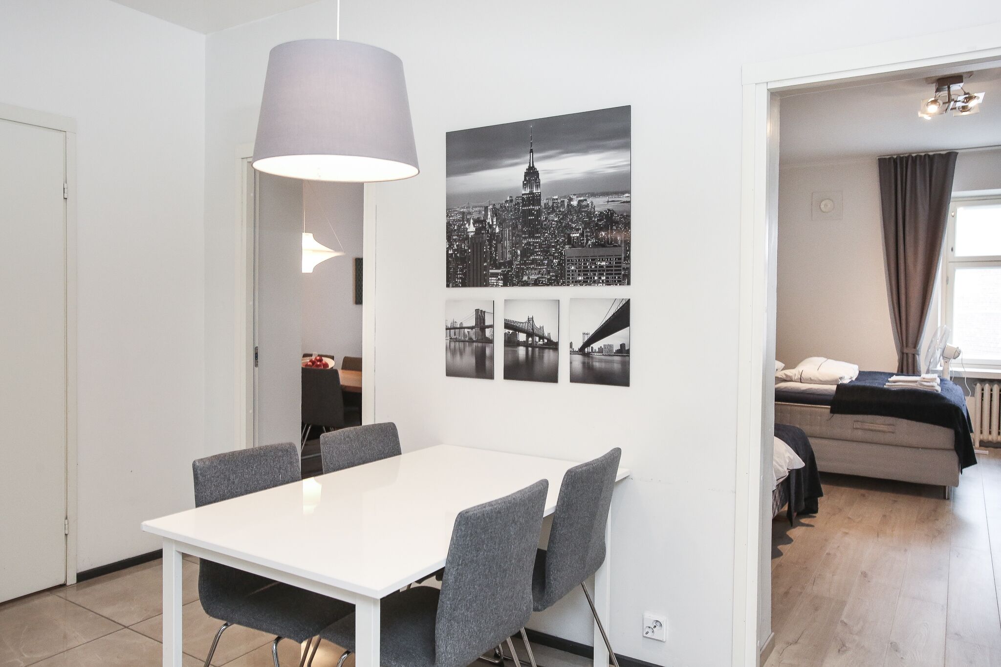 Ett modernt vardagsrum med en vit soffa, ett matbord med grå stolar och ett stort fönster med gardiner.