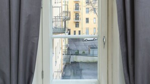 Ein Fenster mit Blick auf ein gelbes Gebäude mit Balkonen und einem darunter geparkten Auto.