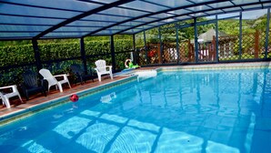 Una piscina interior con agua azul cristalina, rodeada de sillas de plástico blancas y un cerramiento de vidrio.