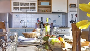 Een keuken met witte kastjes, een betegelde spatwand en een eettafel gedekt met borden, glazen en een fles wijn.