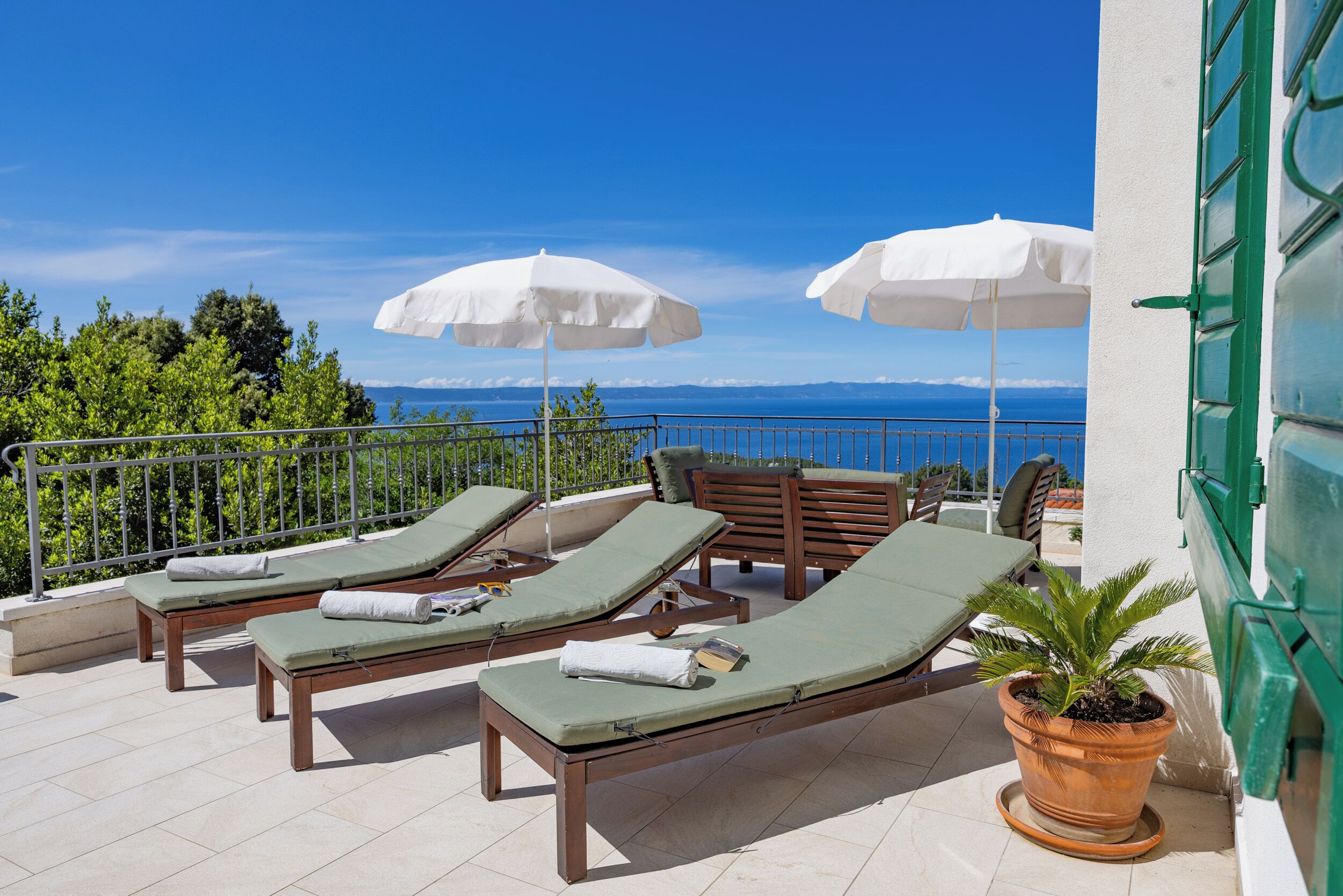 A terrace with sun loungers, umbrellas, and a potted plant.