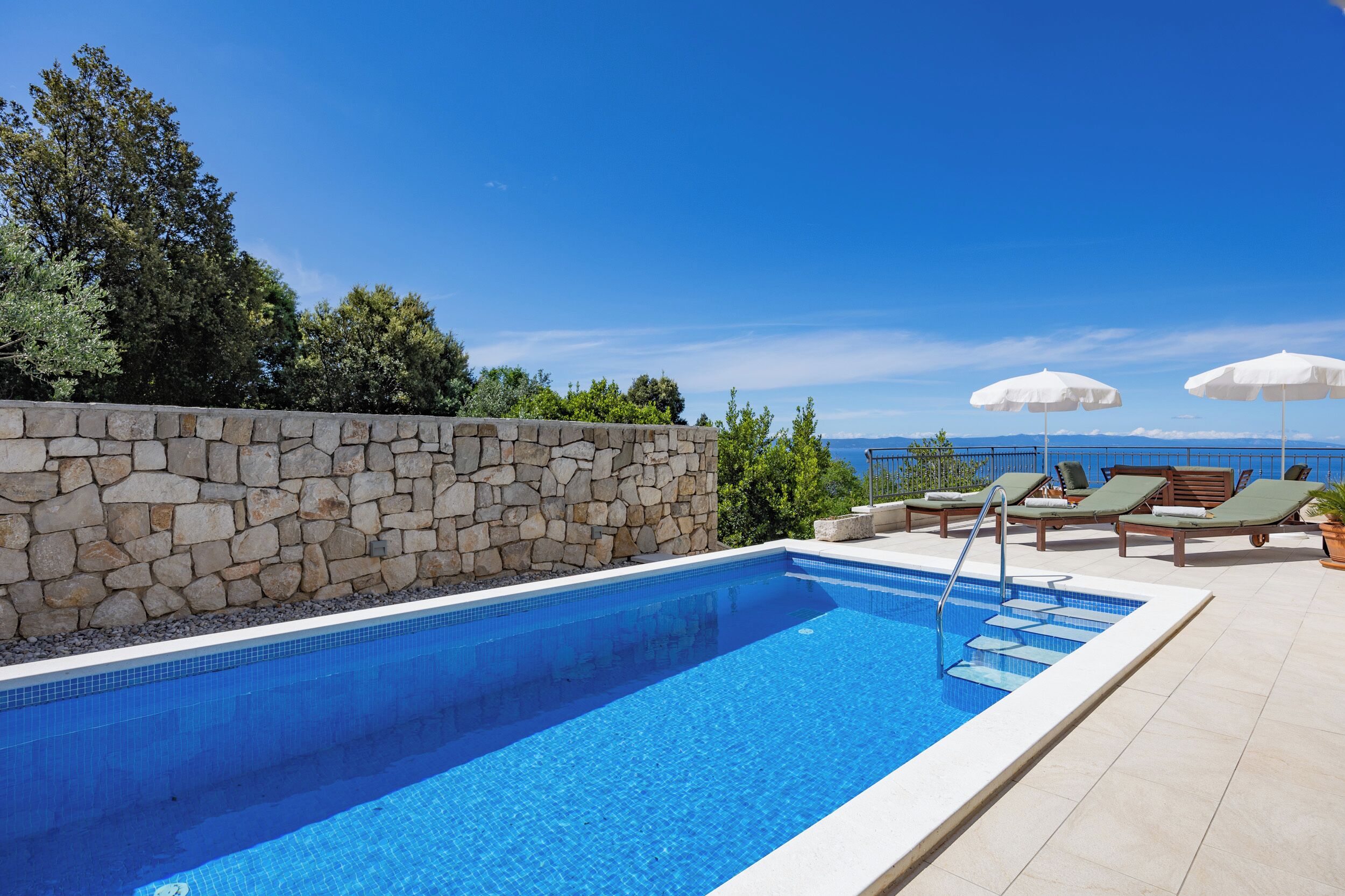 Une piscine avec des murs en pierre, des chaises longues et des parasols.