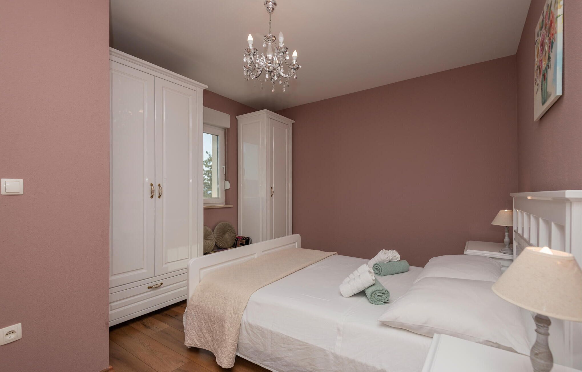 A bedroom with a large bed, a chandelier, a wardrobe, and a painting on the wall.